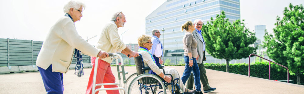 A group of older adults walking together outside in downtown Denver. Some of the people are using mobility devices, like a wheelchair and a walker.