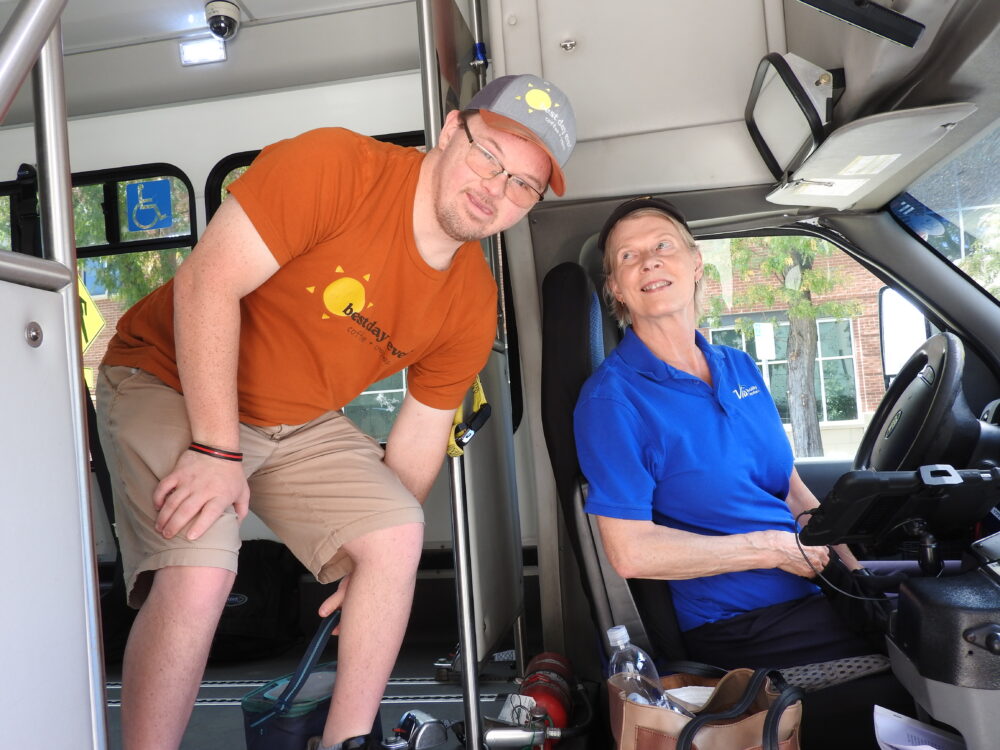 Seth, a Via Mobility Services rider, leaning into a Via bus beside a smiling Via Mobility Services driver