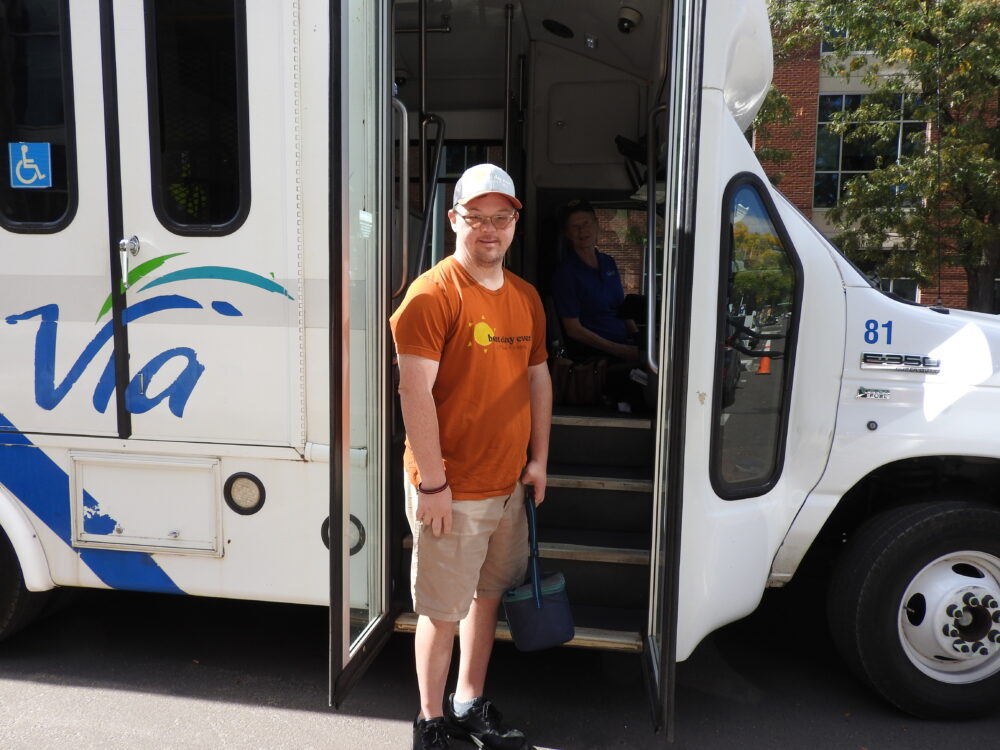 Seth, a Via Mobility Services rider, standing at the door of a Via bus with a Via Mobility Services driver inside